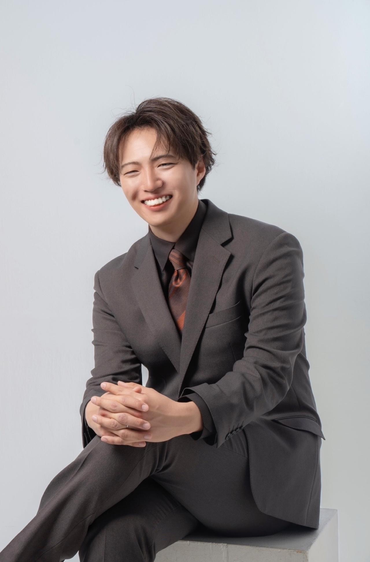 ダークスーツ姿で座り、笑顔を見せるOrange U代表・川端佑典
